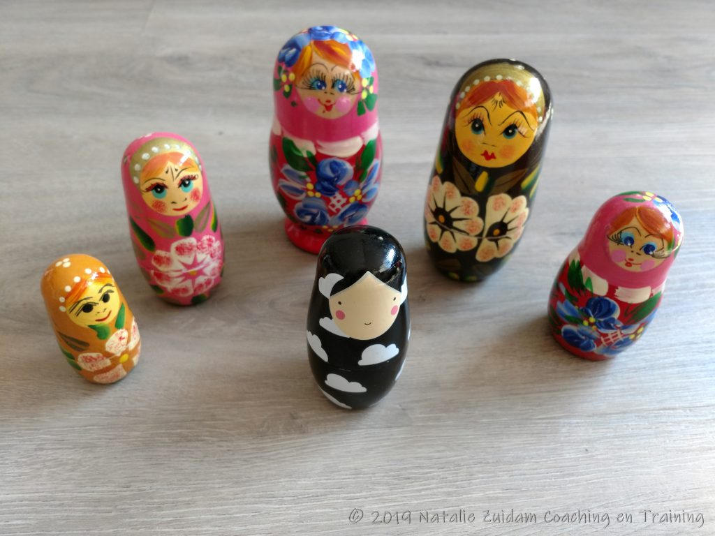 Een zwartwitte babushka met daaromheen in een halve cirkel vijf gekleurde Babushka's van verschillende grootte